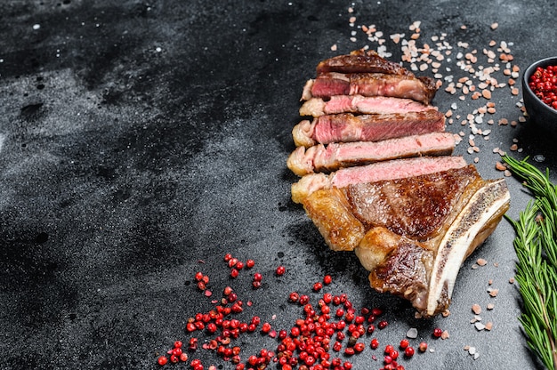 Bife de lombo com osso com sal e pimenta. carne de vaca grelhada. fundo preto. vista do topo. copie o espaço.