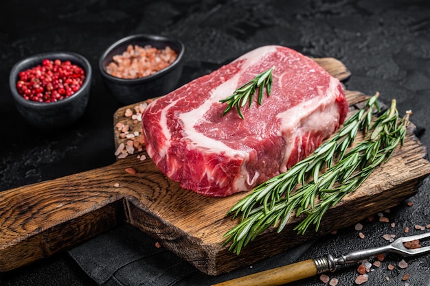 Bife de lombo cru, carne marmorizada de carne na placa de madeira com alecrim. Fundo preto. Vista do topo.