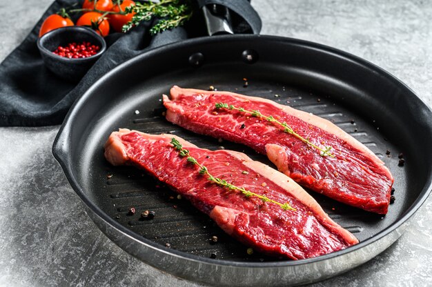 Bife de lombo de tira crua em uma panela de grelha, ingredientes para cozinhar. Fundo cinza. Vista do topo