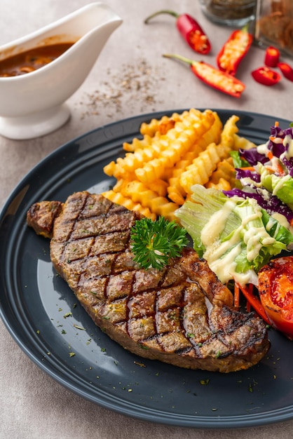 Bife de lombo grelhado com batatas fritas e saladas. Sirva em Prato Preto. Espaço negativo.