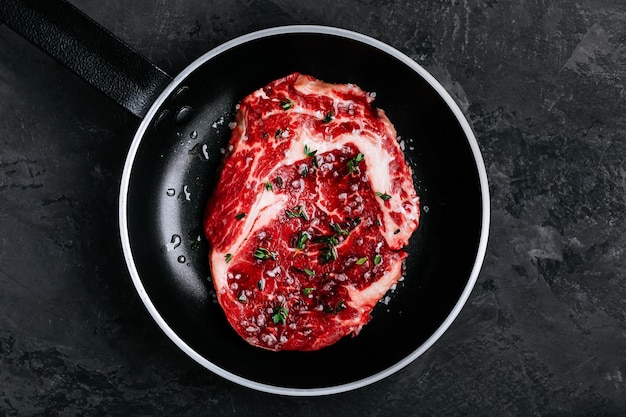 Foto bife de olho de costela fresco cru em frigideira sobre fundo de pedra escuro preparado para cozinhar grelha de churrasco espaço de cópia de vista superior