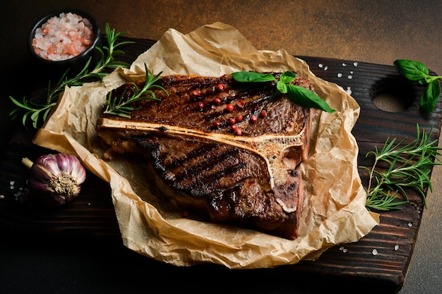 Foto bife de osso com alecrim em papel de pergaminho bife de carne em fundo escuro carne