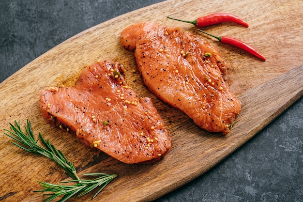 Bife de peru marinado em uma placa de madeira com alecrim e pimenta.