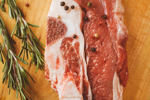 Bife de porco com alecrim e pimenta em um fundo de madeira Processamento de fotos vintage de bife de carne crua