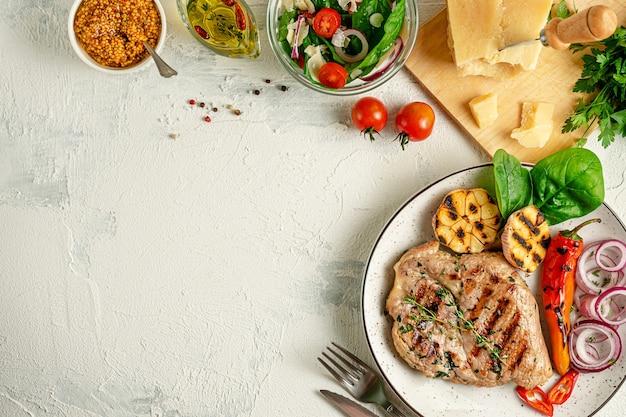 Bife de porco grelhado caseiro com legumes, especiarias e queijo parmesão no fundo de concreto