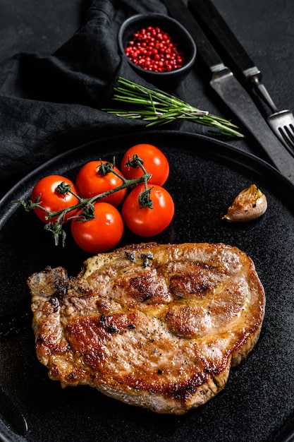 Bife de porco grelhado no osso com tomates. Fundo preto. Vista do topo