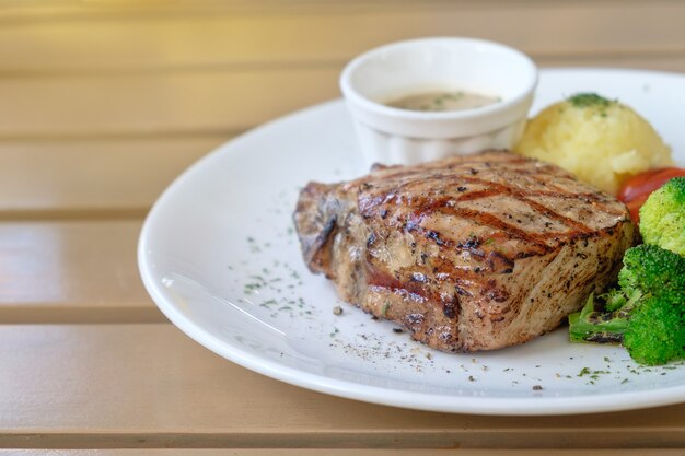 Bife de porco grelhado suculento com tomate de brócolis e purê de batata em chapa branca