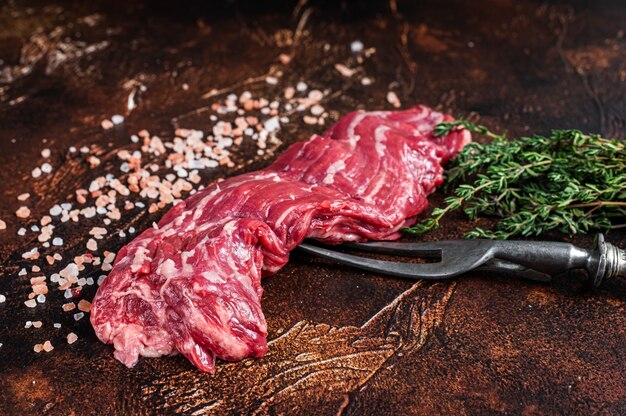 Bife de saia machete cru no garfo de carne. Fundo escuro. Vista do topo.