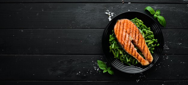 Bife de salmão assado com feijão verde em um prato preto. Vista do topo. Espaço de cópia grátis.