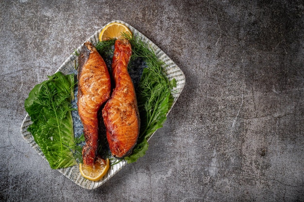 Bife de salmão assado com limão, salada e endro e salsa em um prato contra uma mesa de pedra cinza