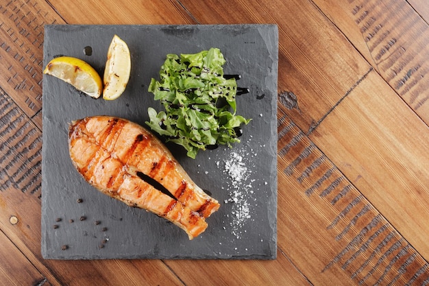 Bife de salmão com limão e verduras em uma superfície de ardósia. fundo de madeira