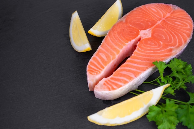 Bife de salmão cru com limão e salsa em fundo preto com espaço de cópia