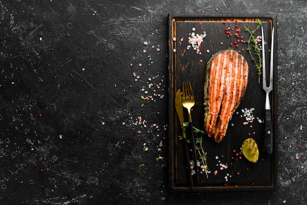 Bife de salmão delicioso cozido fresco com especiarias e ervas assadas em uma placa preta vista superior com espaço para copiar texto