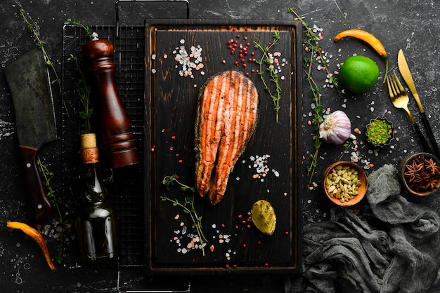 Bife de salmão delicioso cozido fresco com especiarias e ervas assadas em uma placa preta. Vista superior com espaço para copiar texto.