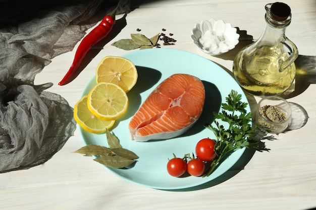 Bife de salmão fresco com ingredientes na placa azul e fundo branco de madeira