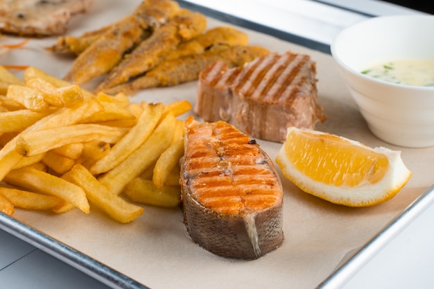 Bife de salmão grelhado com limão e fritas na luz de fundo.