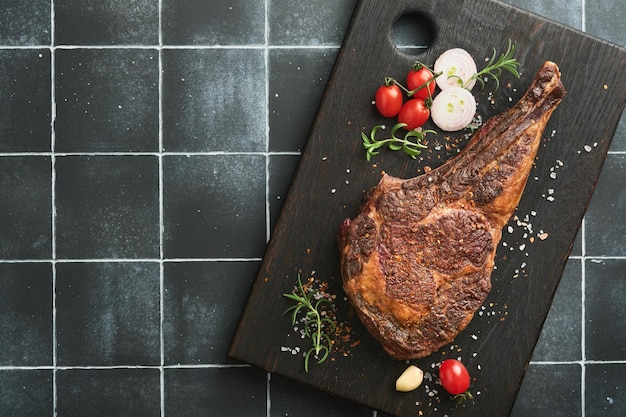 Bife de tomahawk Bife de tomahawk grelhado fatiado com ervas de tomate cereja assadas e sal em fundo de madeira velho Preparando-se para grelhar Vista superior e espaço para cópia