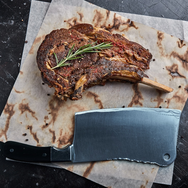 Foto bife de tomahawk com legumes e uma faca em cima da mesa. carne grelhada com legumes grelhados e legumes frescos em cima da mesa.