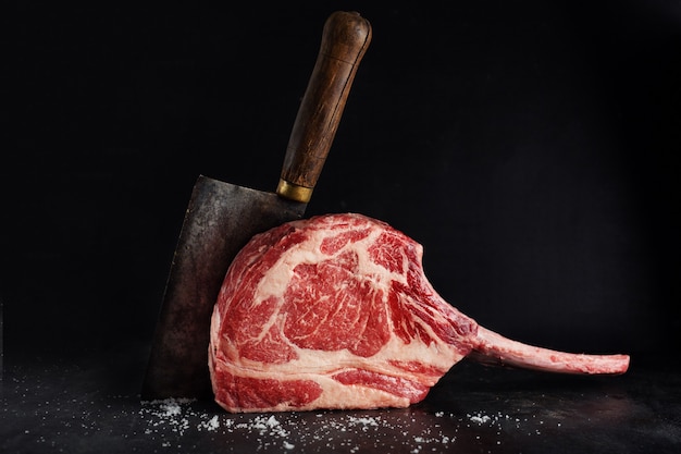 Bife de tomahawk de carne fresca na prancha de madeira velha. fundo escuro. fechar-se