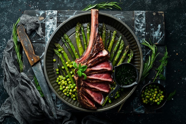 Bife de Tomahawk no osso Bife grelhado com aspargos e ervilhas verdes Em um fundo preto Vista superior Espaço para cópia grátis