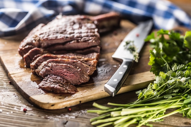 Bife de tomahawk recém grelhado na placa de ardósia com ervas de alecrim e salsa de pimenta. Pedaços de bife suculento.