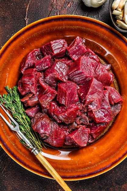 Bife de veado em cubos para goulash de veado. Mesa escura. Vista do topo.