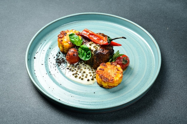 Bife de vitela quente com vegetais grelhados tomates de milho e pimenta em um prato pratos de restaurante em um fundo de pedra escura