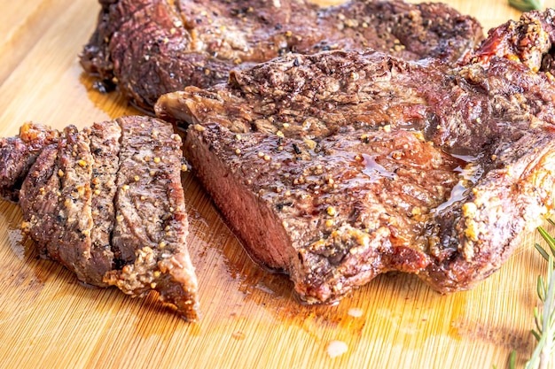 Bife do lombo assado cortado em bifes em uma tábua de madeira sobre uma mesa de madeira Com alecrim e tomate