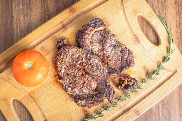 Bife do lombo assado cortado em bifes em uma tábua de madeira sobre uma mesa de madeira Com alecrim e tomate