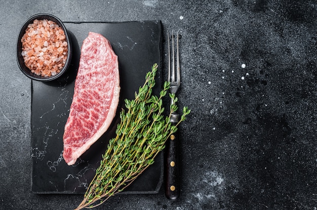 Bife do lombo cru wagyu, carne de boi kobe no tabuleiro de mármore. fundo preto. vista do topo. copie o espaço.