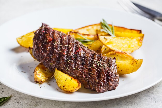 Bife e fatias de batata cozida com alecrim em chapa branca.