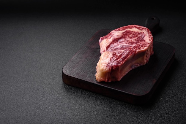 Bife fresco e suculento de carne crua com sal e especiarias sobre um fundo escuro de concreto