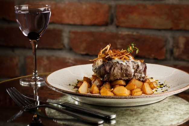 Bife grelhado com batatas douradas assadas servidas com cebola crocante em cima sobre um fundo de tijolos Receita deliciosa