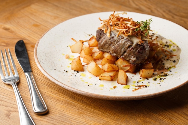 Bife grelhado com batatas douradas assadas servidas com cebola crocante em cima sobre um fundo de tijolos receita deliciosa