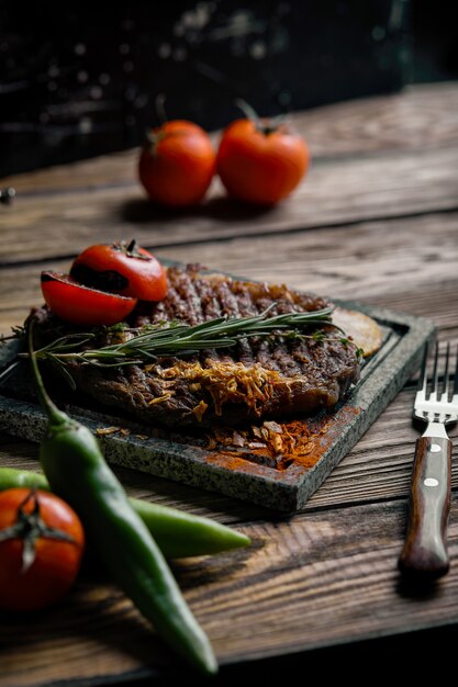 Bife grelhado com faca e garfo esculpido na ardósia de pedra preta. bife em uma pedra de mármore quente. copie o espaço, fundo escuro, foto de moda de alimentos.