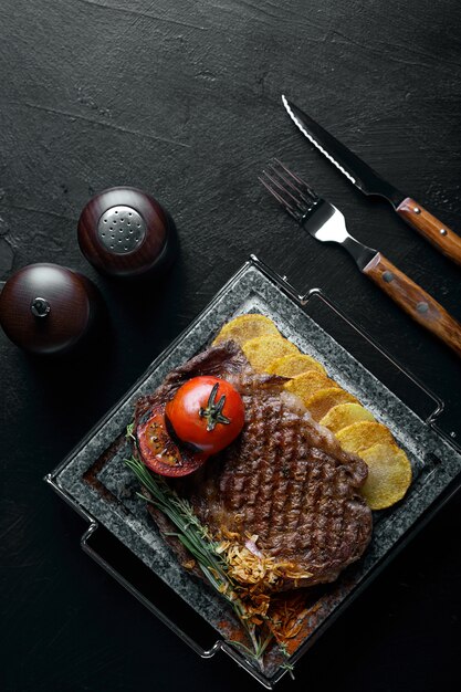 Bife grelhado com faca e garfo esculpido na ardósia de pedra preta. Bife em uma pedra de mármore quente.