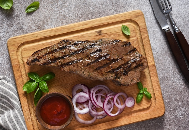 Bife grelhado com molho de tomate e cebola roxa em conserva em uma placa de madeira. vista de cima.