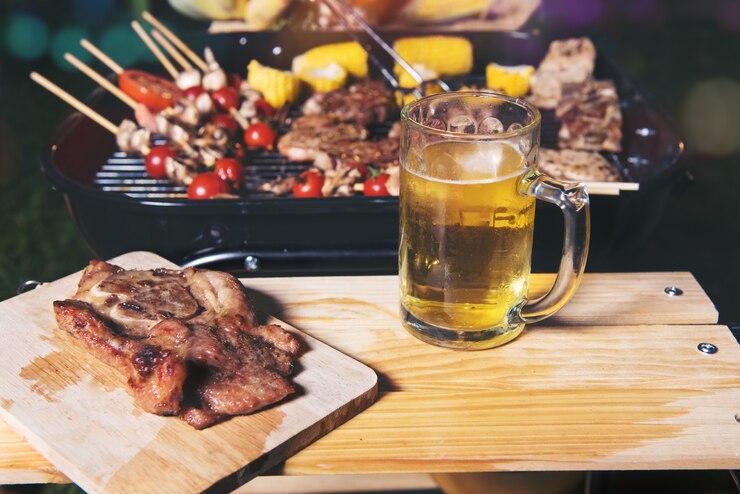 Bife grelhado com tomate e milho na tábua e caneca de cerveja na mesa de madeira