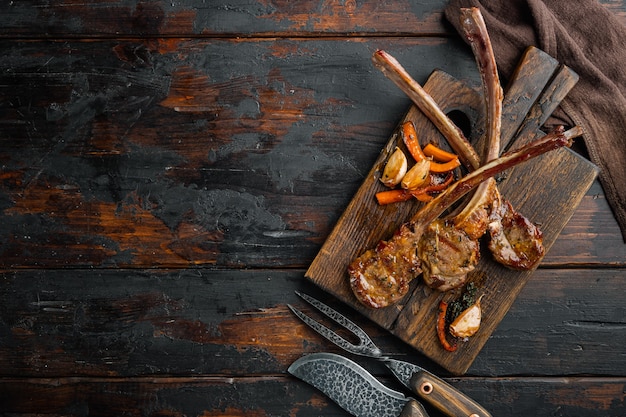 Bife grelhado de carne de cordeiro cortado em fatias com vegetais, óleo e espécies definidas, em uma tábua de servir de madeira, na velha mesa de madeira escura, vista de cima plana lay