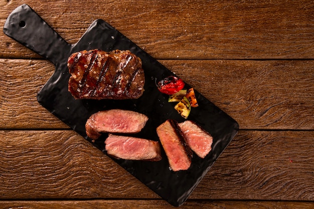 Bife grelhado em fatias em uma placa de corte preta sobre a mesa de madeira.