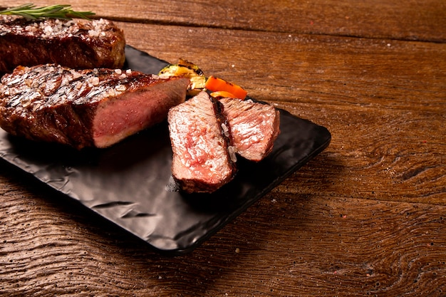 Bife grelhado em fatias em uma placa de corte preta sobre a mesa de madeira.