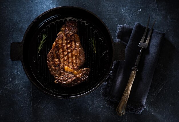 Bife grelhado em uma panela de ferro fundido e garfo para carne, vista superior