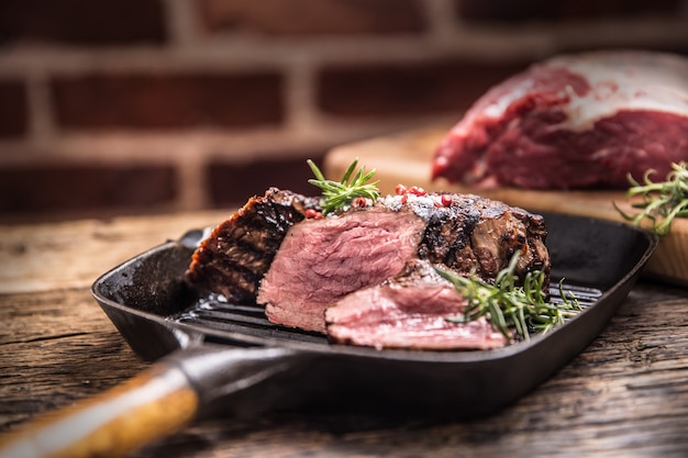 Bife grelhado na grelha com alecrim de ervas na mesa de madeira.