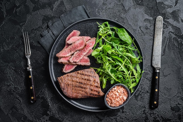 Bife grelhado para churrasco em um prato com salada verde Fundo preto Vista superior