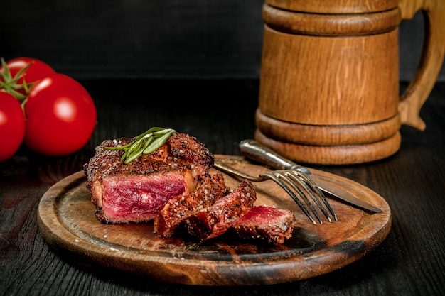 Bife grelhado temperado com especiarias e ervas frescas servido em uma tábua de madeira com uma caneca de cerveja de madeira ...