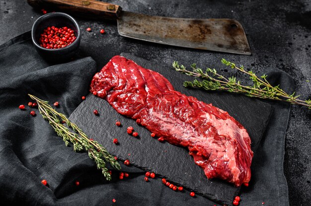 Bife marmorizado cru com pimenta rosa e tomilho. superfície preta. vista do topo