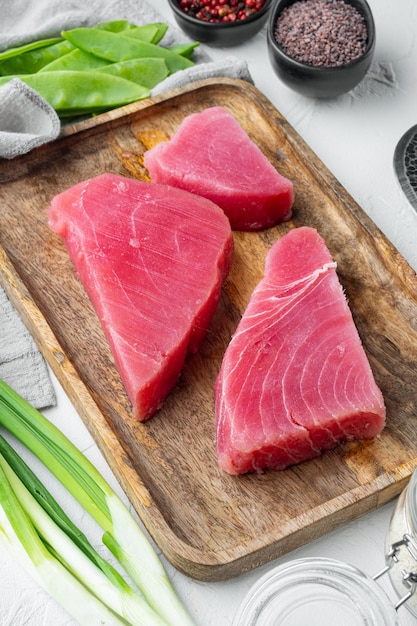 Bife orgânico cru de filé de atum com conjunto de ingredientes, na bandeja de madeira, sobre fundo de pedra branca