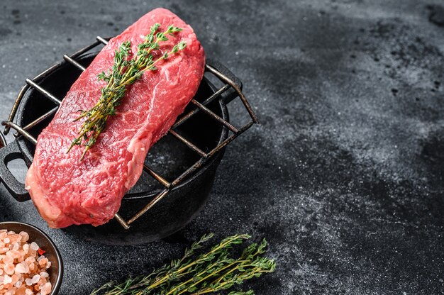 Bife Striploin cru na grelha, carne marmorizada. Fundo preto. Vista do topo. Copie o espaço.