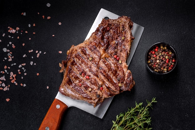 Bife suculento delicioso com especiarias e ervas em um fundo escuro de concreto. Pratos grelhados