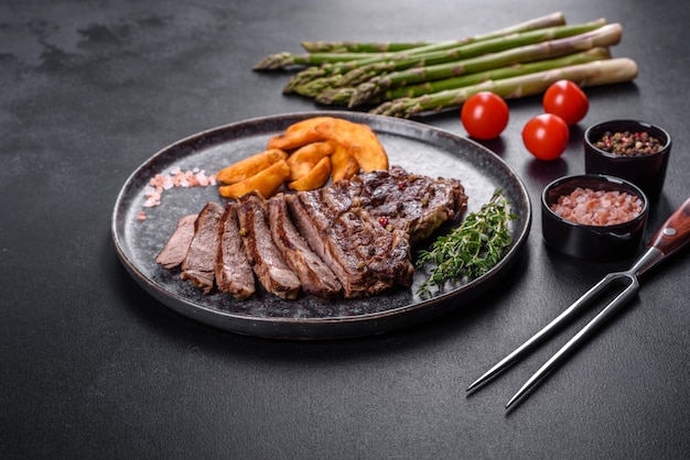 Bife suculento delicioso com especiarias e ervas em um fundo escuro de concreto. Pratos grelhados